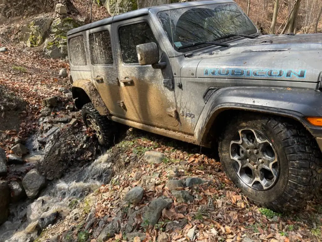 Jeep Wrangler Rubicon off-road vehicle crosses a stream on a forest path.